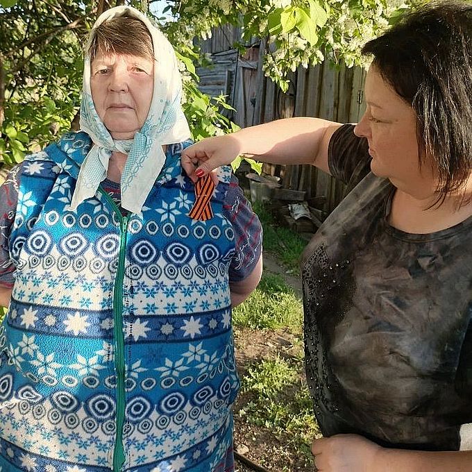 Социальный работник прикалывает Георгиевскую ленточку пожилой женщине