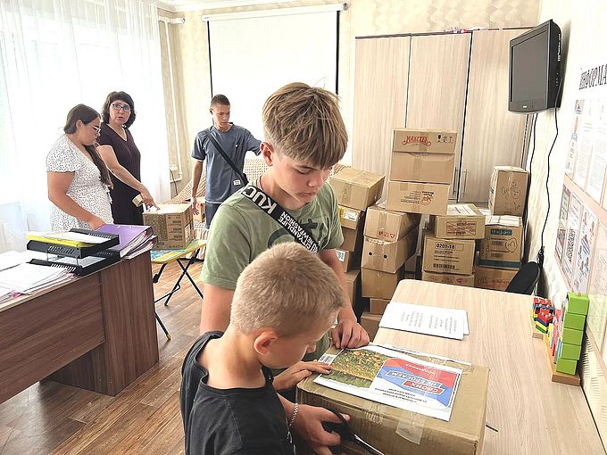 Два мальчика приклеивают скотчем к посылке изображение «Своих не бросаем»