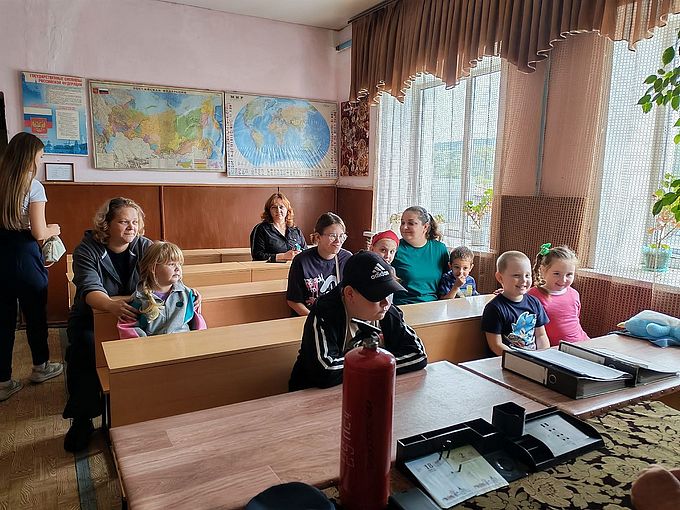 Дети и их родители сидят за партами в кабинете пожарной части