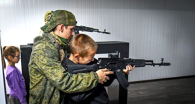 Инструктор показывает мальчику как держать автомат